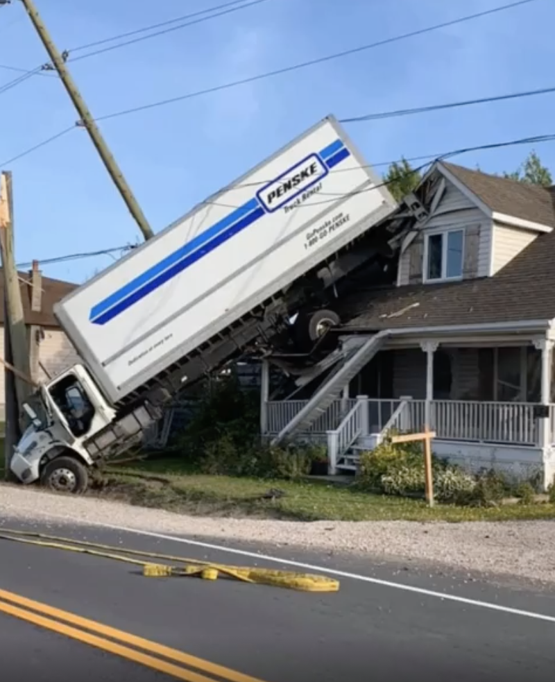 A Penske moving truck is lifted off the ground, crashed into the side of a house, causing structural damage. Power lines are down nearby
