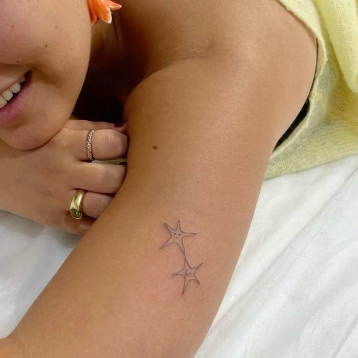 Mujer acostada mostrando un pequeño tatuaje de dos estrellas en el brazo