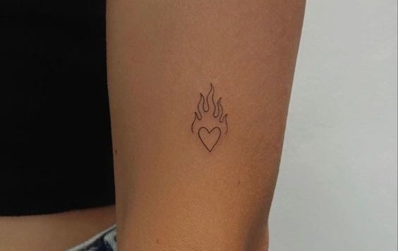 Tatuaje minimalista de un corazón con llamas en el antebrazo de una persona