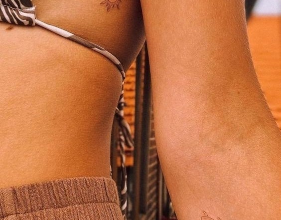 Dos personas con tatuajes finos: un sol en las costillas de una y una tortuga en el antebrazo de la otra. Ambos llevan ropa veraniega y casual