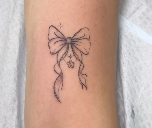 Tatuaje de un lazo con cintas largas y una pequeña flor en el centro, en el brazo de una persona sobre una superficie médica