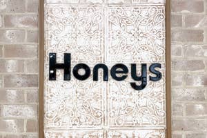 レンガの壁に「Honeys」と書かれたお店の看板。装飾的な背景が特徴。