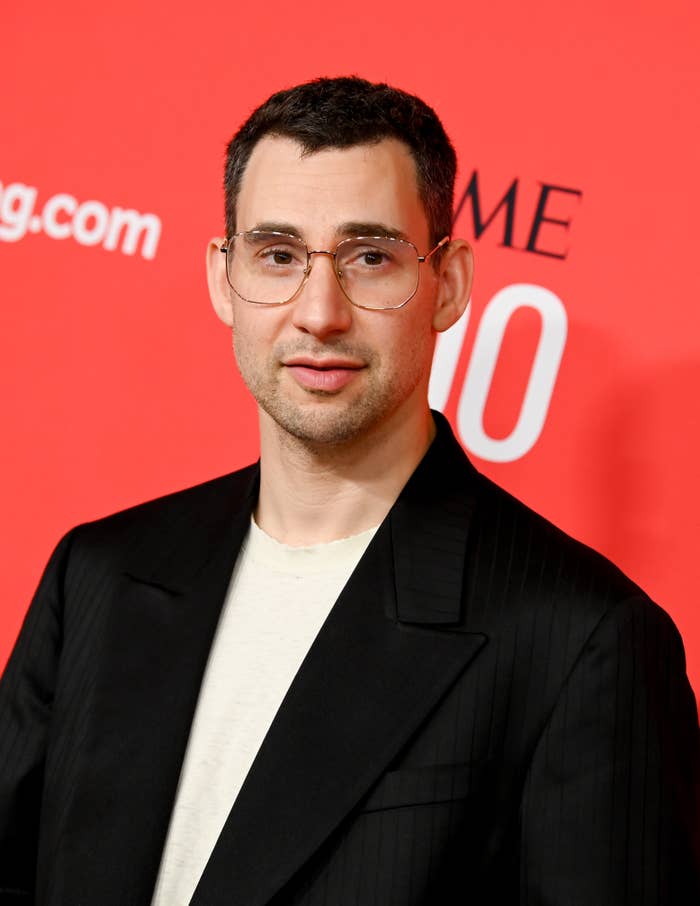 Jack Antonoff on the red carpet, wearing a dark suit jacket over a white shirt, with glasses