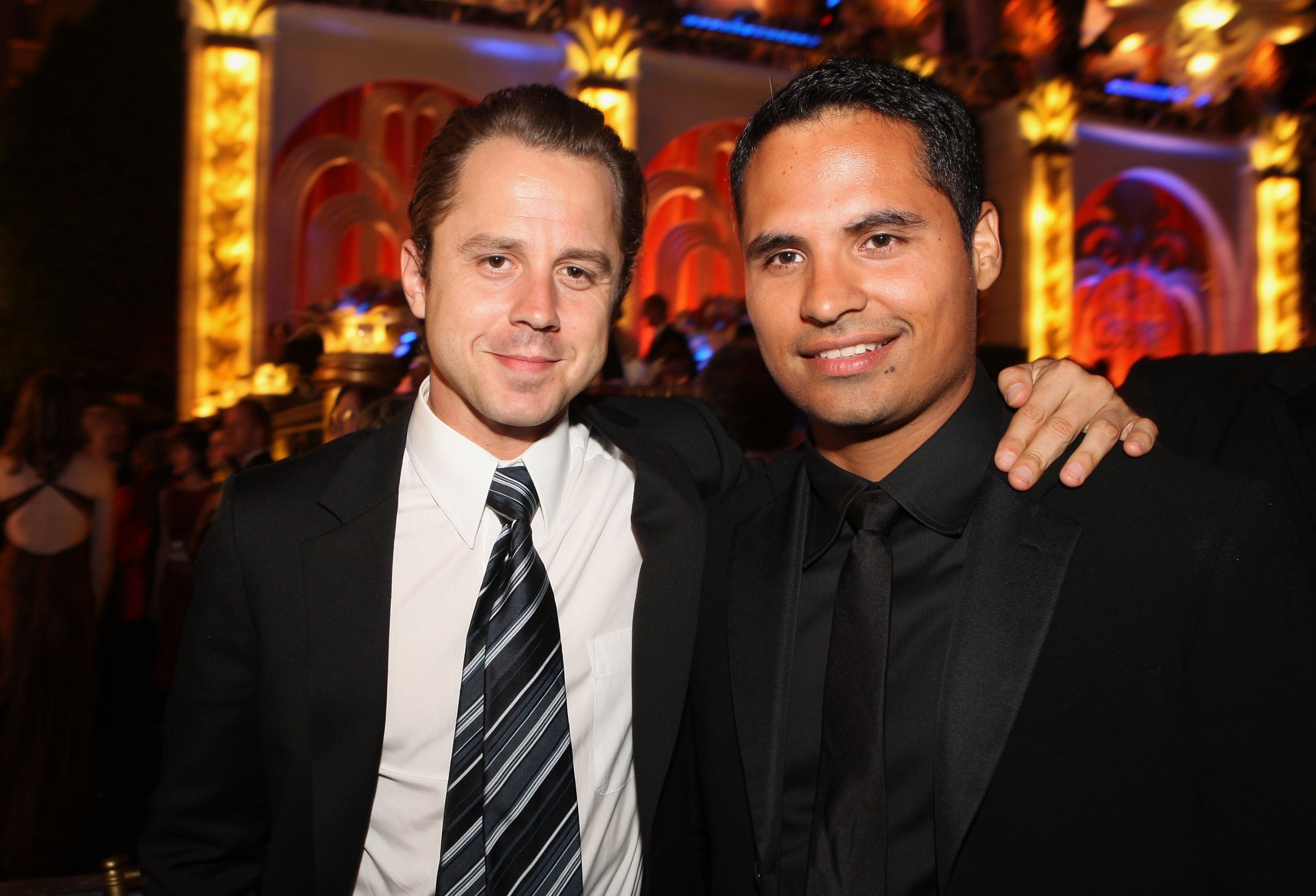 Actors Giovanni Ribisi and Michael Peña, are posing together in suits at an elegant event