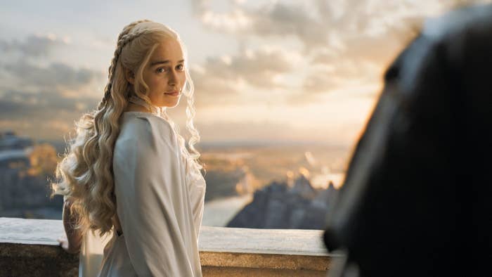 Emilia Clarke as Daenerys Targaryen stands on a balcony, wearing a flowing, elegant dress, looking back over her shoulder with a serene expression