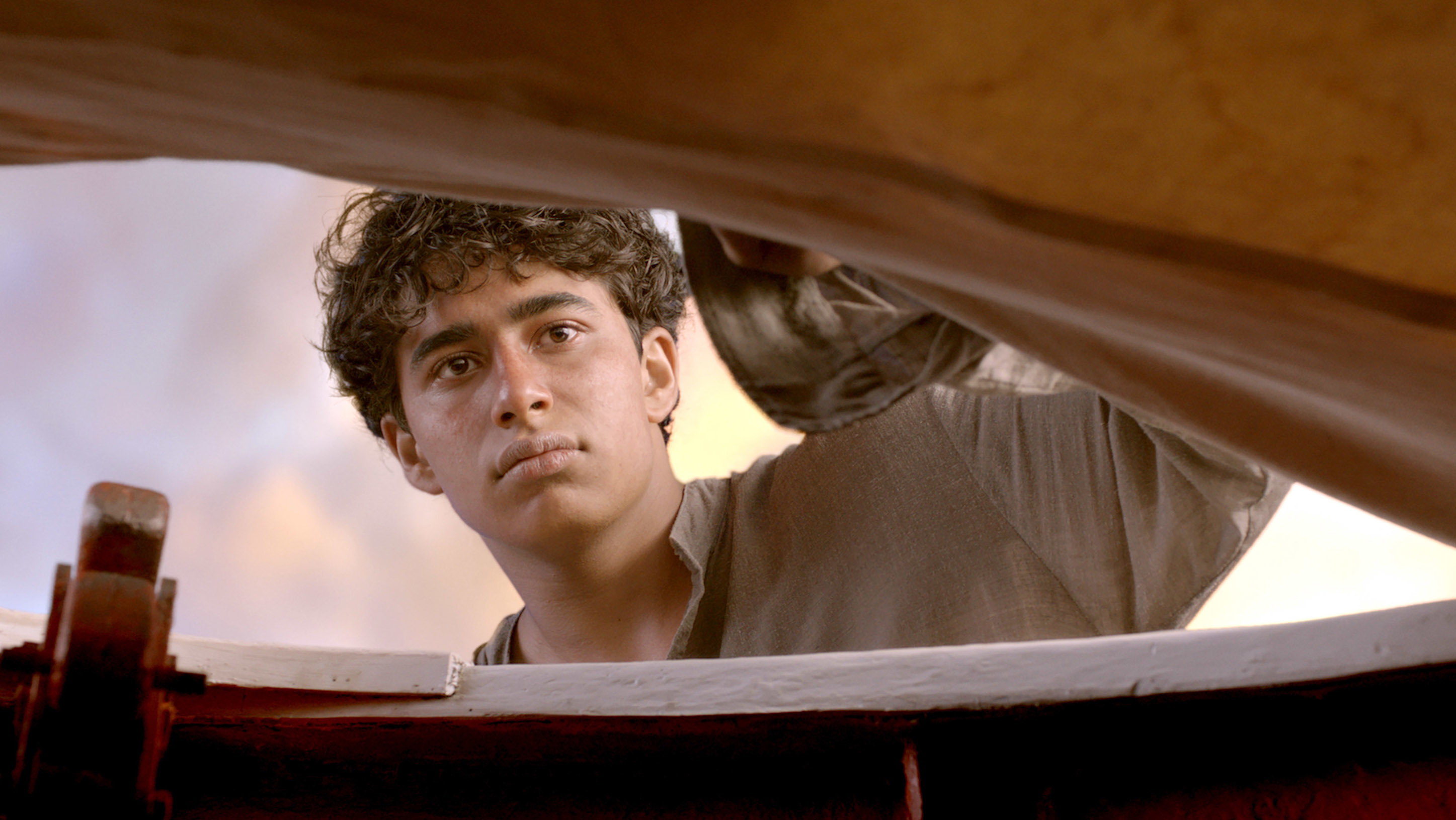 Suraj Sharma, as the character Pi from "Life of Pi," peers down with a curious expression, appearing to look into a lifeboat