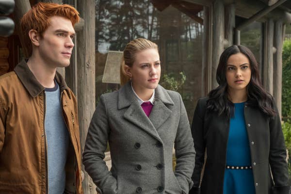KJ Apa, Lili Reinhart, and Camila Mendes stand outside in a forest setting, dressed in casual outdoor winter wear