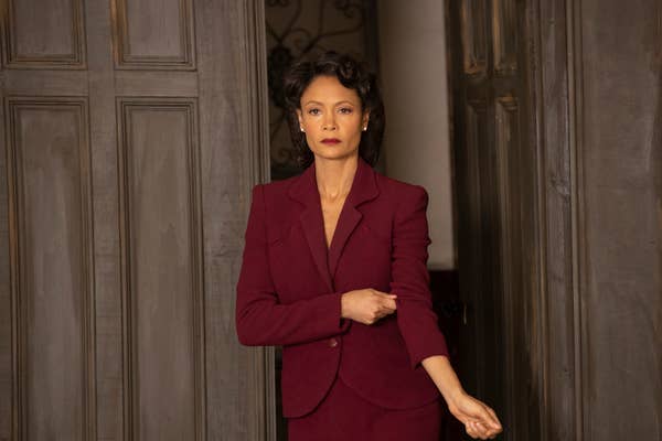 Thandiwe Newton stands in a room wearing a formal suit with a blazer. She has an arm slightly raised, adjusting her sleeve