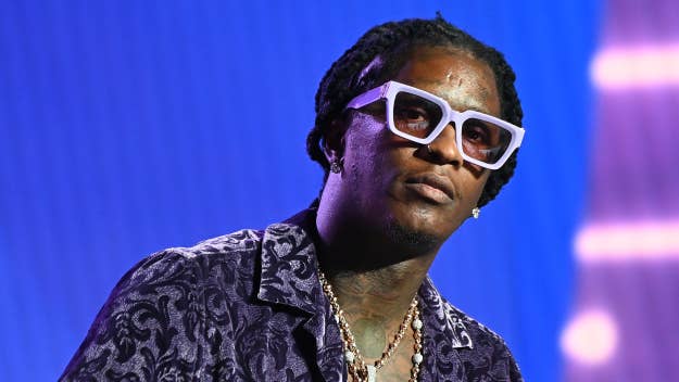 Young Thug on stage, wearing patterned clothing, white-framed sunglasses, and layered necklaces