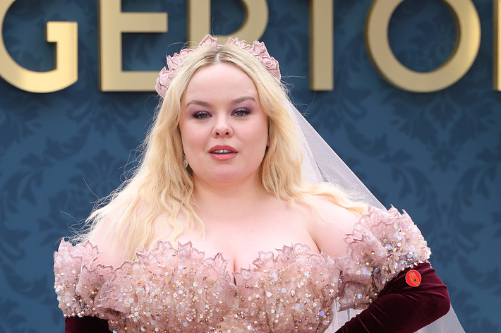 Nicola Coughlan in an off-shoulder, sparkling beaded gown with long velvet gloves and a matching headpiece, posing in front of a &ldquo;Bridgerton&rdquo; backdrop