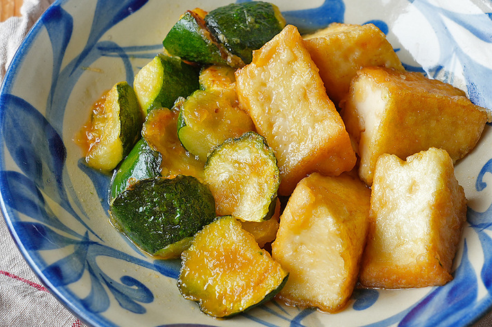 陶器の皿に盛られた揚げた豆腐とズッキーニの料理。