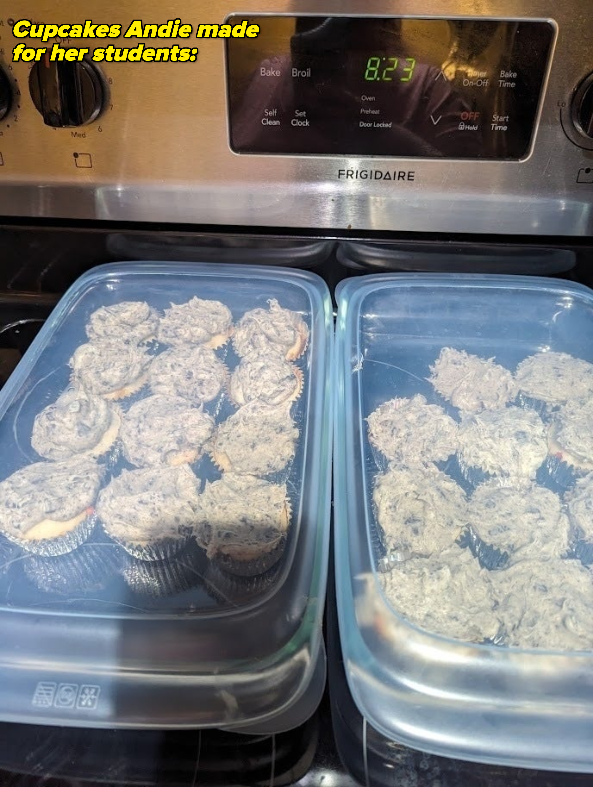 Plastic containers holding cupcakes with frosting are placed on a stove. The time on the stove is 8:23