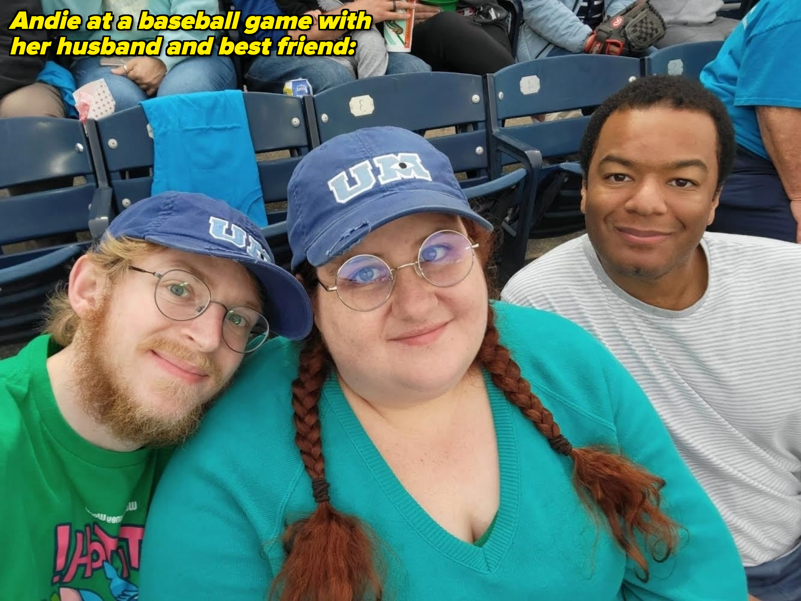 Group selfie at an event: three people, two wearing baseball caps with &quot;UM&quot; and glasses, all smiling and sitting in a stadium