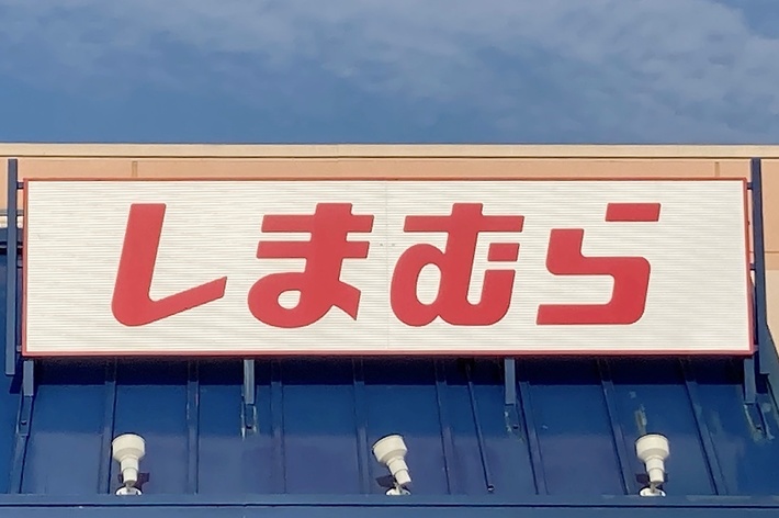 Storefront with a sign in Japanese characters. The sign reads &ldquo;しまむら&rdquo;. There is also an accessible parking sign visible in the lower right corner