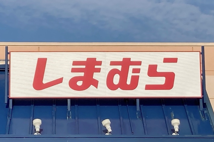 A storefront with a sign above the entrance displaying Japanese text. The building features a blue awning and a handicap parking sign is visible