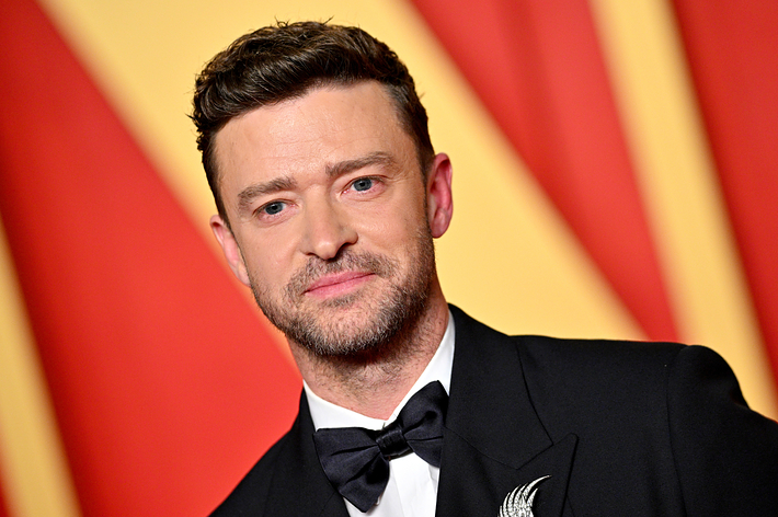 Justin Timberlake in a formal black tuxedo with a bowtie and brooch, smiling at a red carpet event