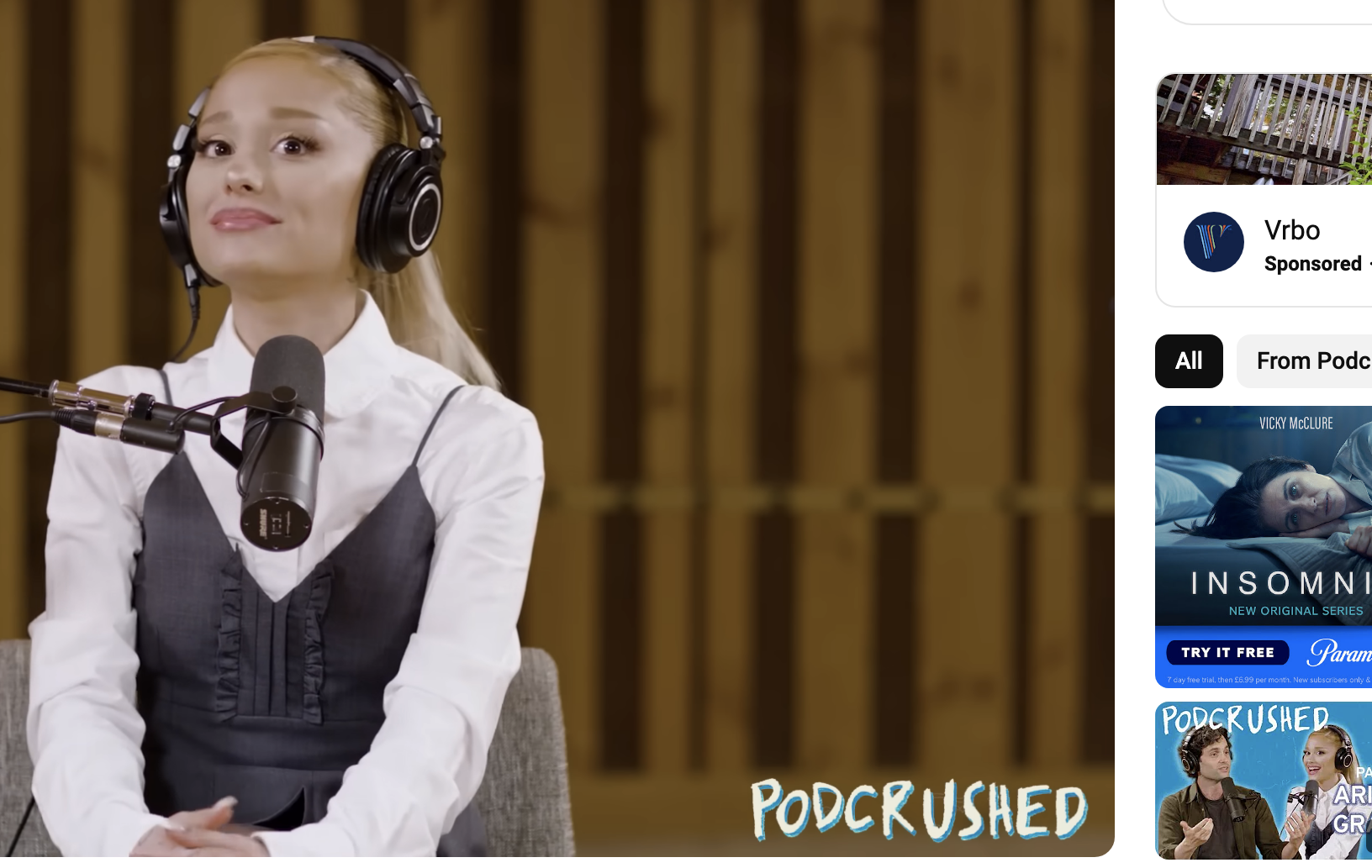 Ariana Grande in an interview, wearing a sleeveless top over a white shirt, speaking into a microphone on the YouTube channel Podcrushed