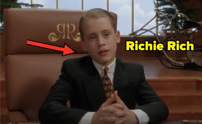 Macaulay Culkin sits at a large desk in a suit and tie, appearing thoughtful and professional in a corporate office setting