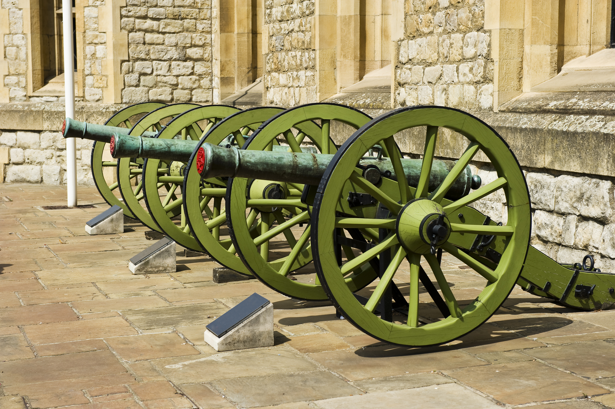Historic green cannons, aligned in a row, displayed outdoors against the Tower of London