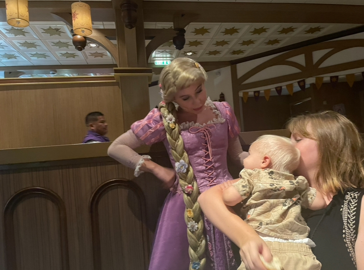 Rapunzel from Frozen meets a woman holding a small child, engaging in a heartwarming moment inside a themed venue
