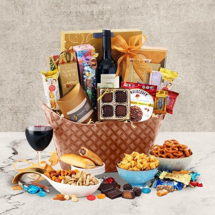 Gift basket with wine, chocolates, cookies, pretzels, popcorn, breadsticks, nuts, and snack bars displayed on a table