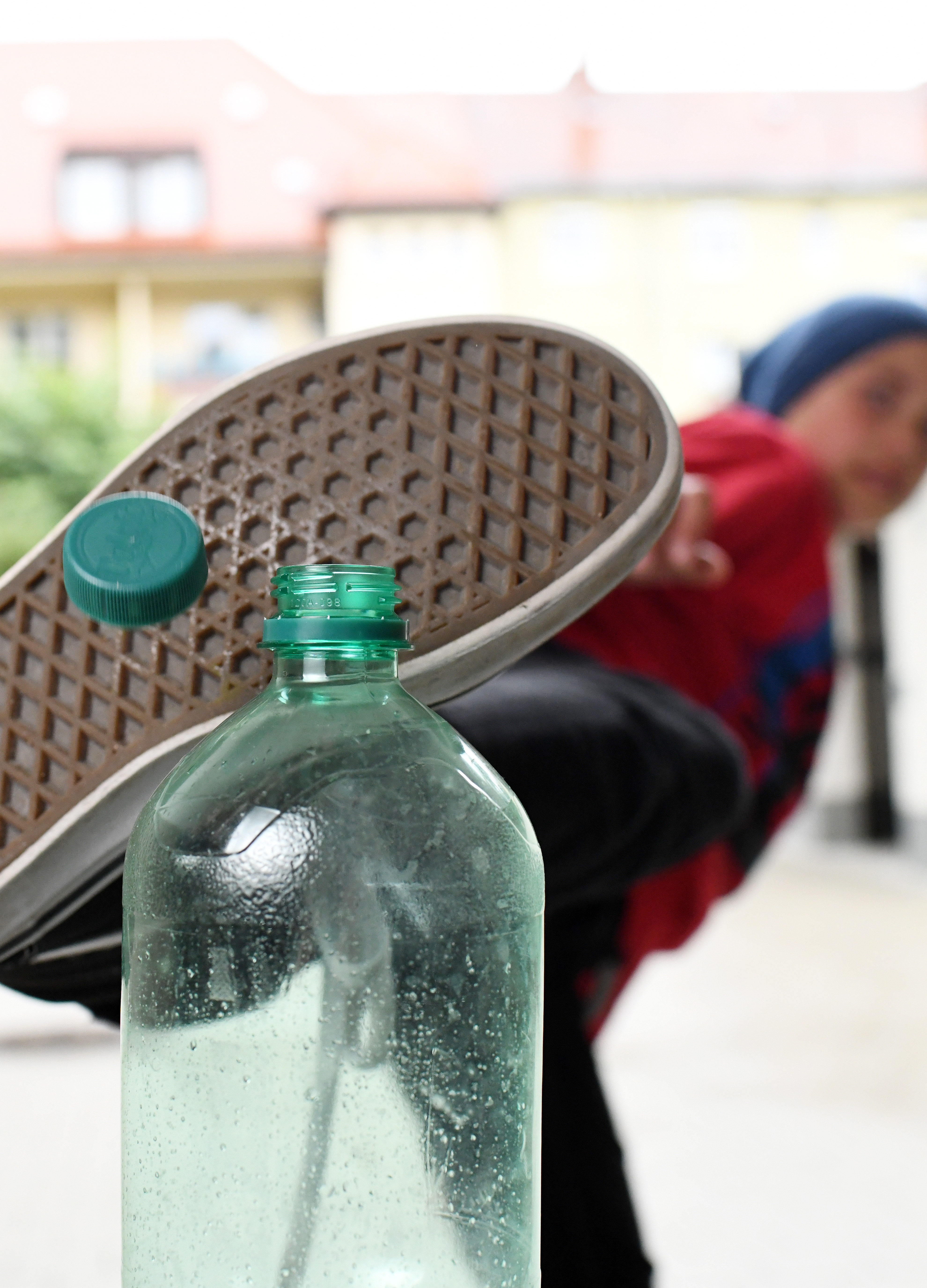 A person in casual clothing performs a bottle cap challenge, kicking a bottle cap off a water bottle. The focus is on the foot and bottle