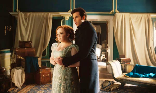 Nicola Coughlan and Luke Newton in period costumes, standing in a vintage room, portraying characters from the TV show &quot;Bridgerton&quot;