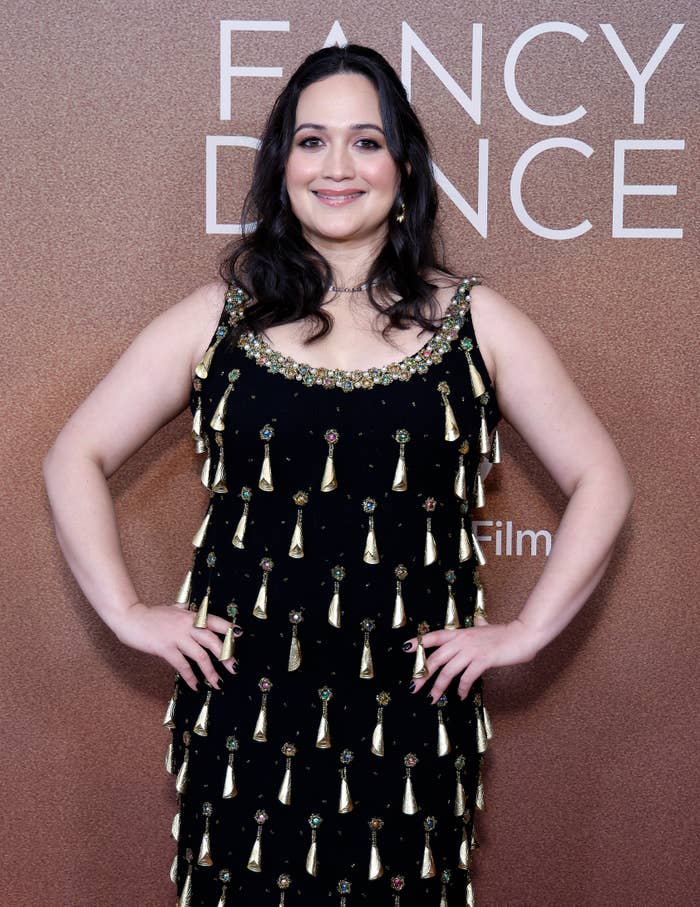 Unknown person on the red carpet with a sleeveless black dress adorned with decorative embellishments, posing in front of a &quot;Fancy Dance&quot; event backdrop