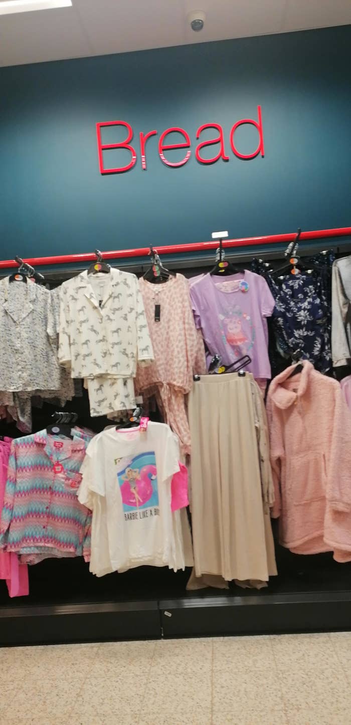 A store section labeled "Bread" with various clothes, including shirts and dresses, hanging underneath the sign