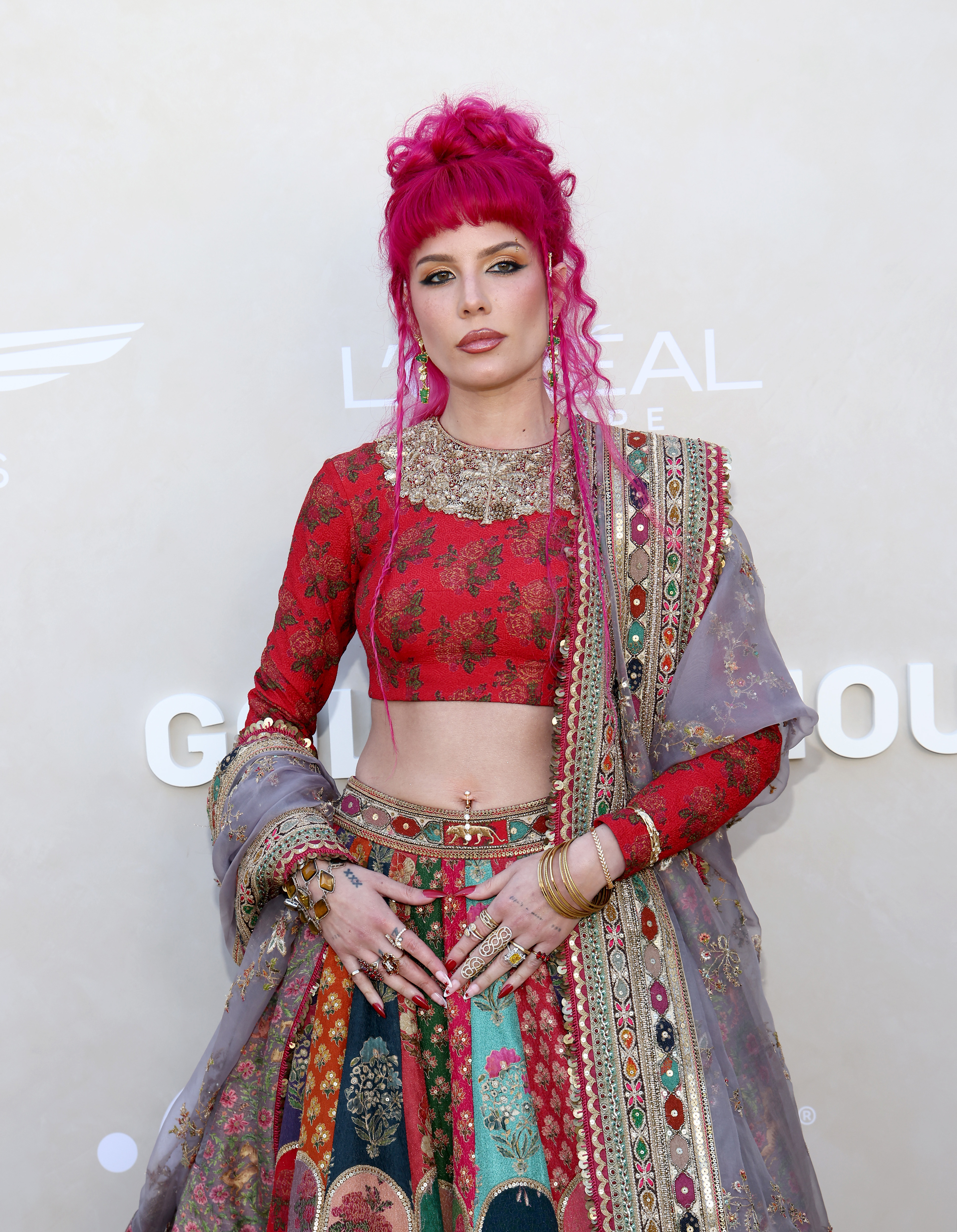 Halsey on the red carpet, wearing an ornate, traditional outfit featuring an embroidered red crop top and a vibrant, multi-colored skirt with elaborate details