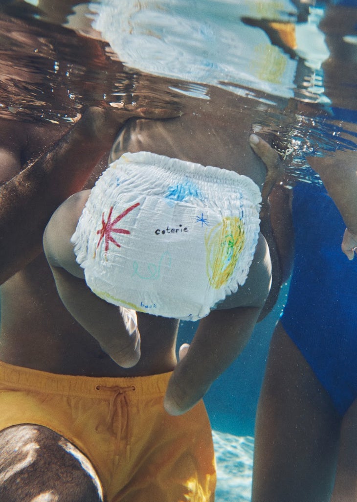 A babe  successful  a diaper with colorful designs is underwater, held by an adult. The big  is wearing yellowish  shorts. The representation  is portion  of a buying  article