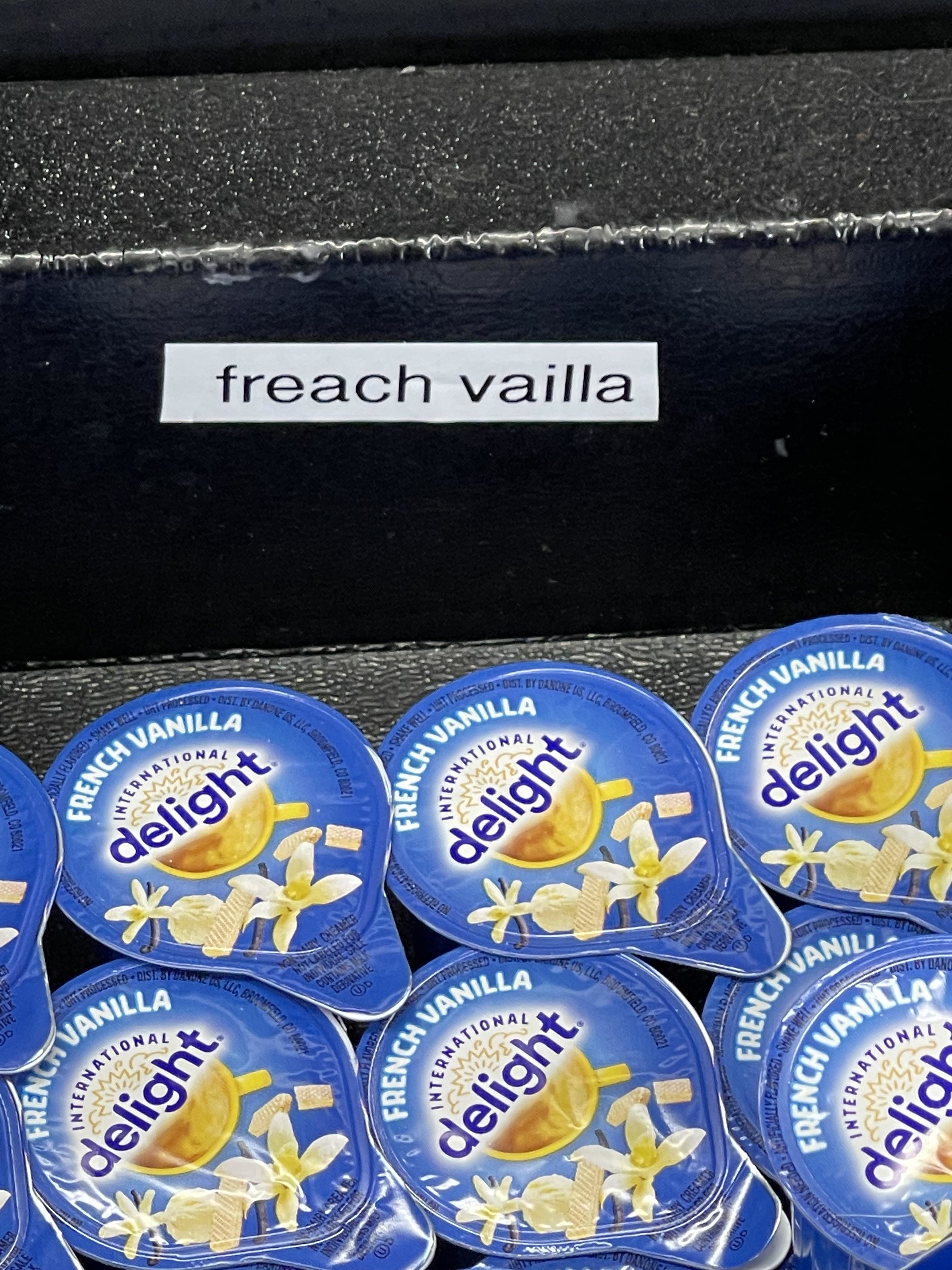 Image of coffee creamer cups labeled "French Vanilla," with a sign mistakenly spelling it as "freach vailla."