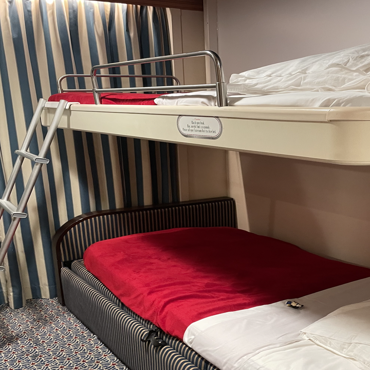 Bunk beds in a room with privacy curtains and striped walls. The top bunk has a railing and ladder, and both beds are made up with white and red bedding