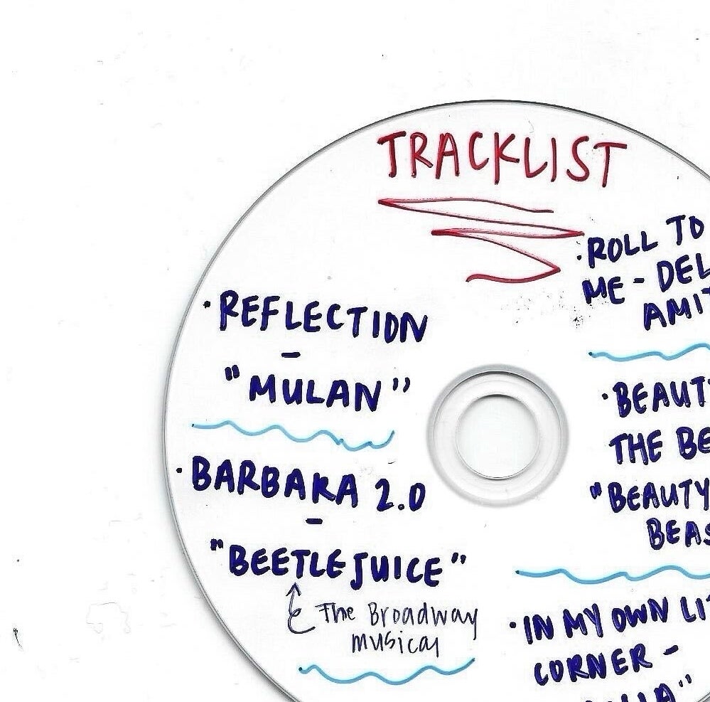 A white CD with a handwritten tracklist including songs: Reflection (Mulan), Barbara 2.0, Beetlejuice (The Broadway Musical), Roll to Me (Del Amitri), Beauty and the Beast, In My Own Little Corner (Cinderella)