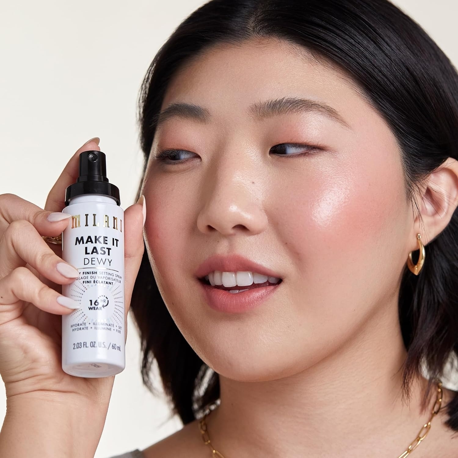 A model holding Milani&#x27;s Make It Last Dewy setting spray close to their face, showing a happy expression
