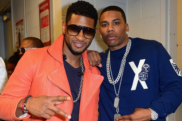 Usher in an orange jacket and sunglasses posing with Nelly in a blue sweatshirt and necklace