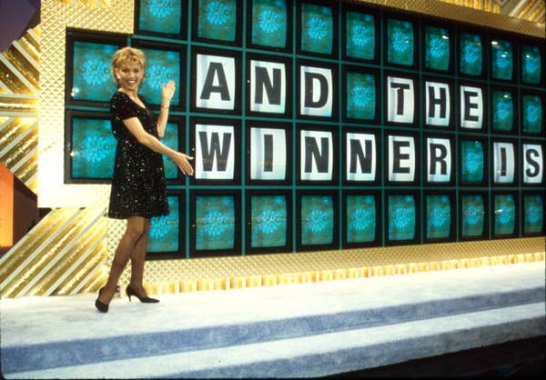 Vanna White in a sparkling dress gestures towards a game board on &quot;Wheel of Fortune&quot; that reads &quot;AND THE WINNER IS&quot;