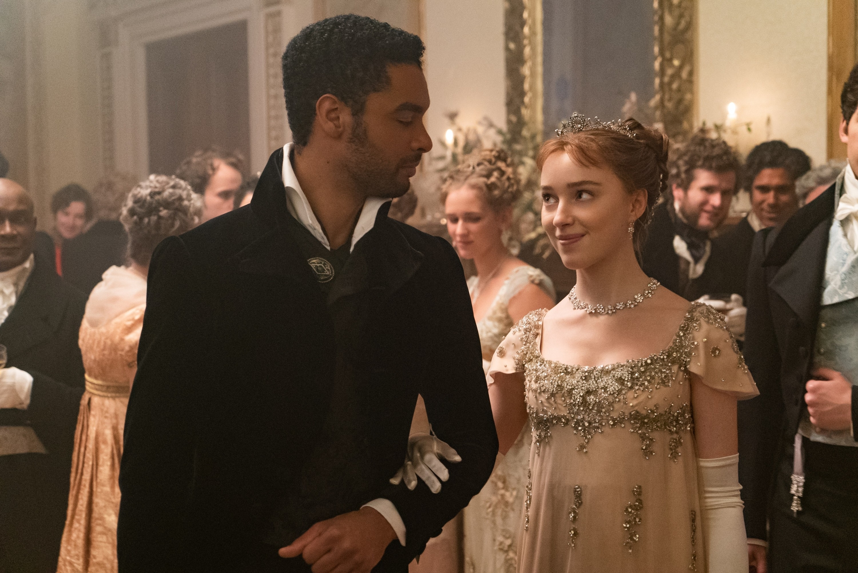 Regé-Jean Page and Phoebe Dynevor in Regency attire at a formal gathering scene from "Bridgerton"
