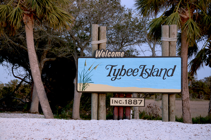 A sign reads "Welcome to Tybee Island Inc. 1887" with palm trees and a beach scene in the background