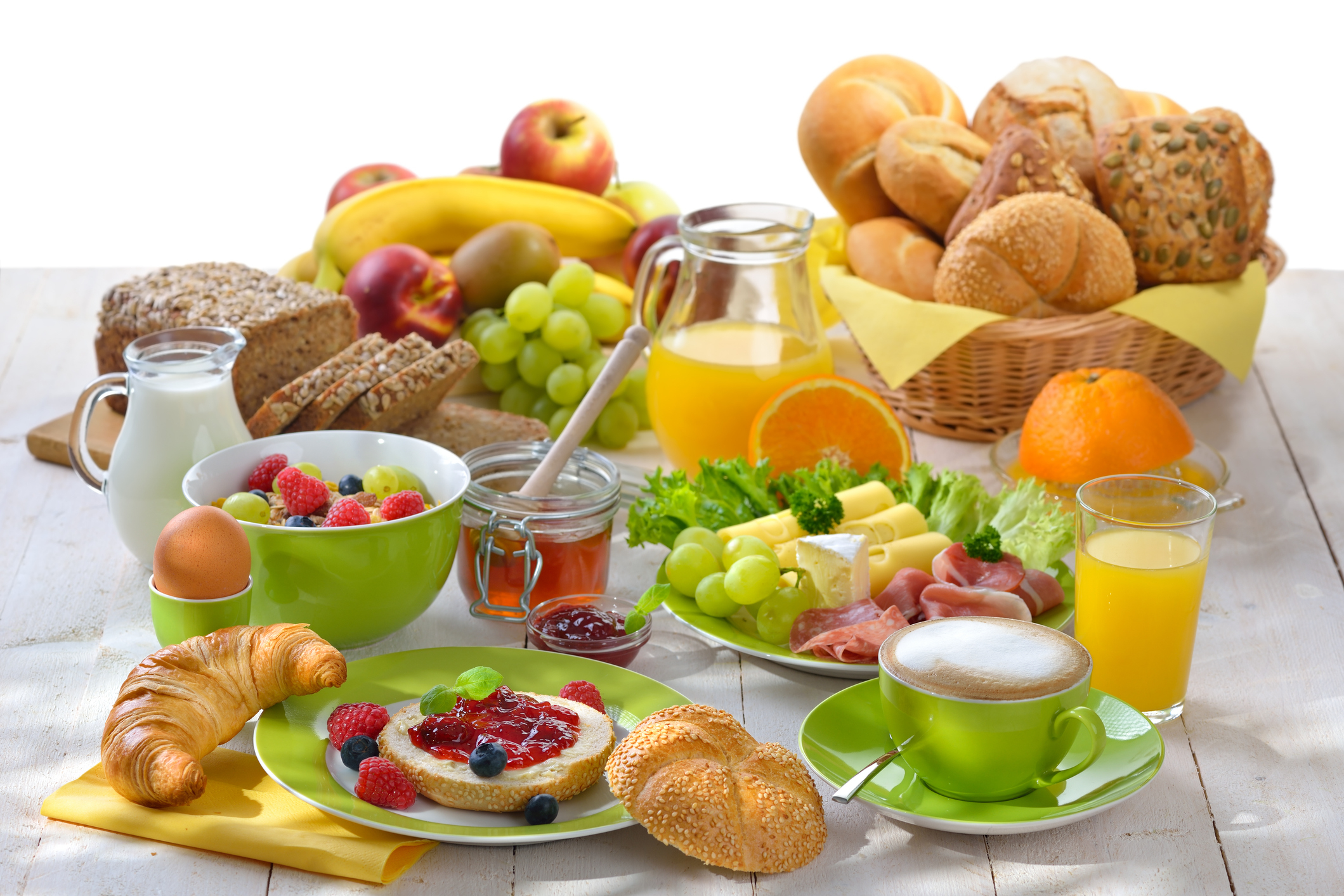 A hearty breakfast spread featuring an assortment of breads, pastries, fruits, cheeses, cured meats, and beverages, including milk, juice, and coffee