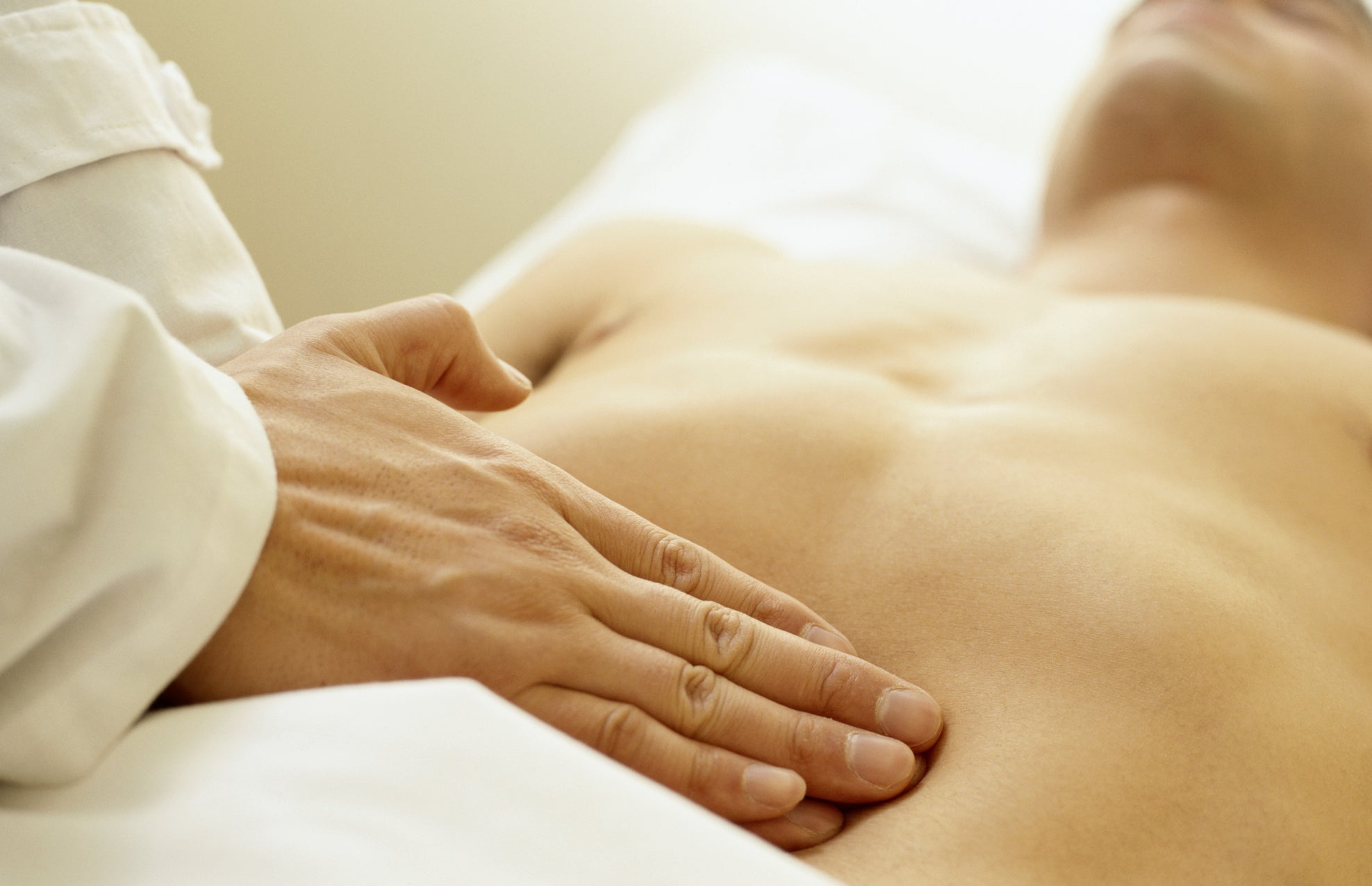 A person lying down receives a physical examination as the doctor's hand gently presses their abdomen