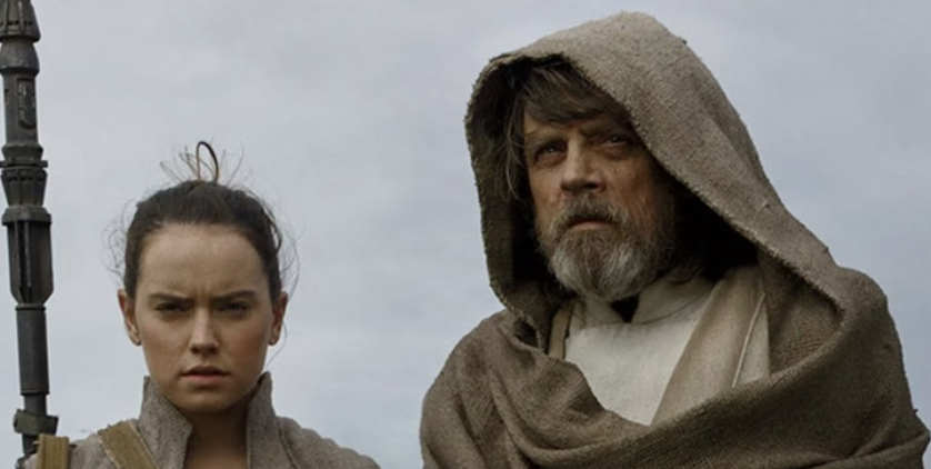 Daisy Ridley, holding a staff, and Mark Hamill in hooded, medieval-style clothing, stand together with serious expressions against a cloudy sky