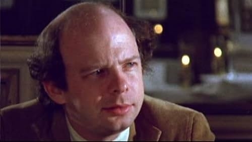 Bald man with light facial hair in a brown jacket, appearing to be in a dimly lit indoor setting