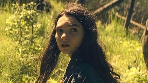Young person with long, dark hair looks over their shoulder in a wooded area