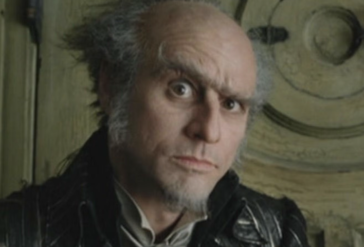 Count Olaf from "A Series of Unfortunate Events" stares intently with a slightly raised eyebrow, wearing a textured black jacket