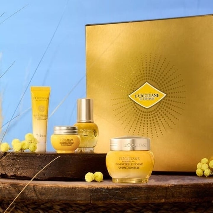 L'Occitane gift set including a tube of cream, a small jar, a pump bottle, and a larger jar, all displayed against a blue background with decorative elements