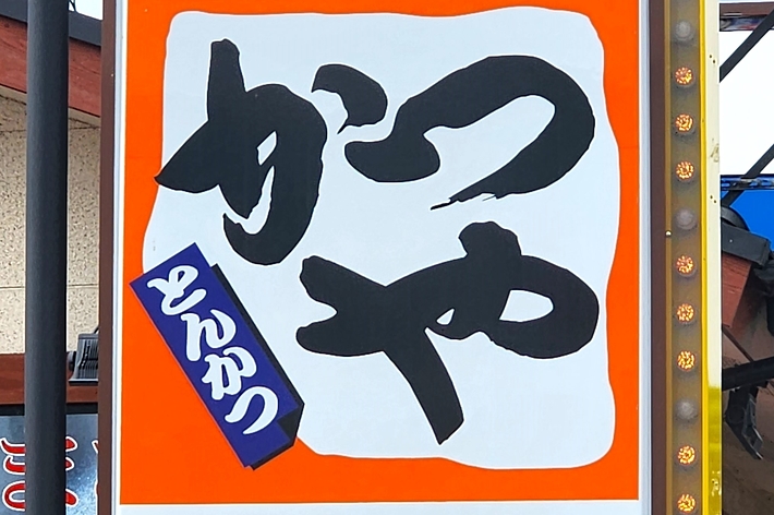 A Japanese restaurant sign advertising pork cutlet rice bowls for 540 yen, with a prominent red arrow pointing to a parking area