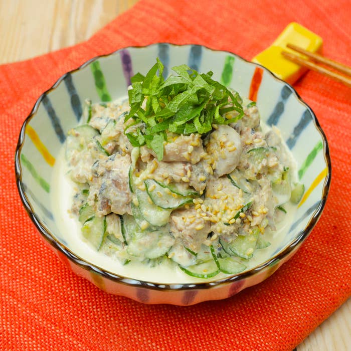 小鉢に盛られたクリーミーなサラダ。キュウリ、ゴマが含まれており、上に刻んだ緑の葉が載っています。