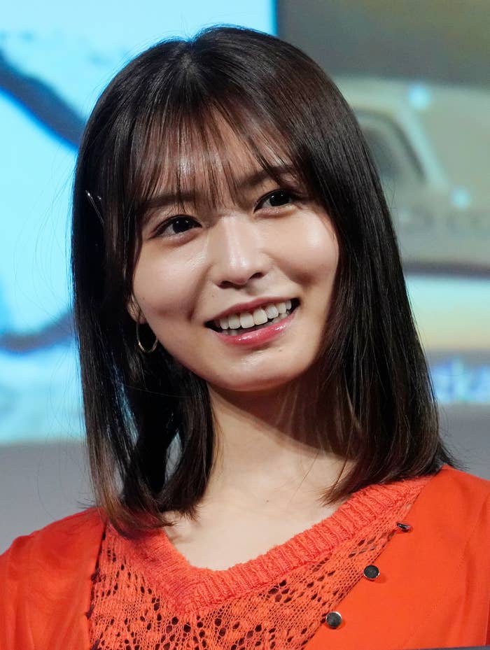 笑顔の女性。赤い服を着ており、前髪があり、肩にかかる長さの髪型。