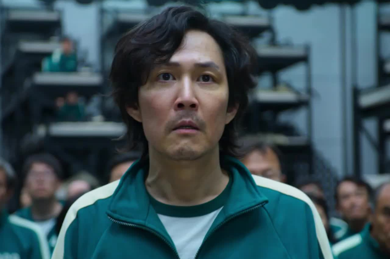 Lee Jung-jae as Seong Gi-hun, in a green tracksuit, looks concerned among a crowd in a scene from "Squid Game."